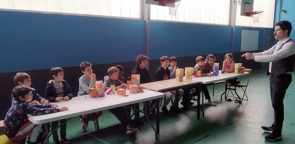 Alain Ackermann anime un atelier de magie auprès d'un groupe d'enfants assis à table